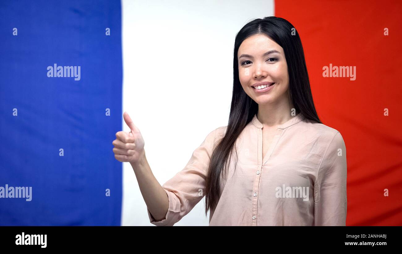 Felice femmina Asiatica che mostra pollice in su contro la bandiera francese sfondo, template Foto Stock