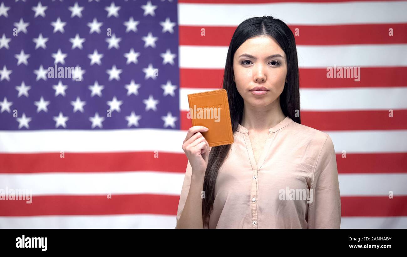 Fiducioso donna asiatica mostrando passaporto contro bandiera degli Stati Uniti sullo sfondo, migrazione Foto Stock