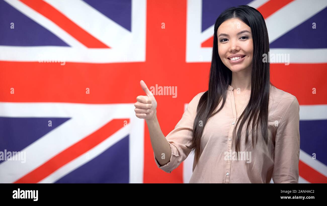 Bella donna che mostra pollice in su contro la bandiera britannica, sfondo modello Foto Stock