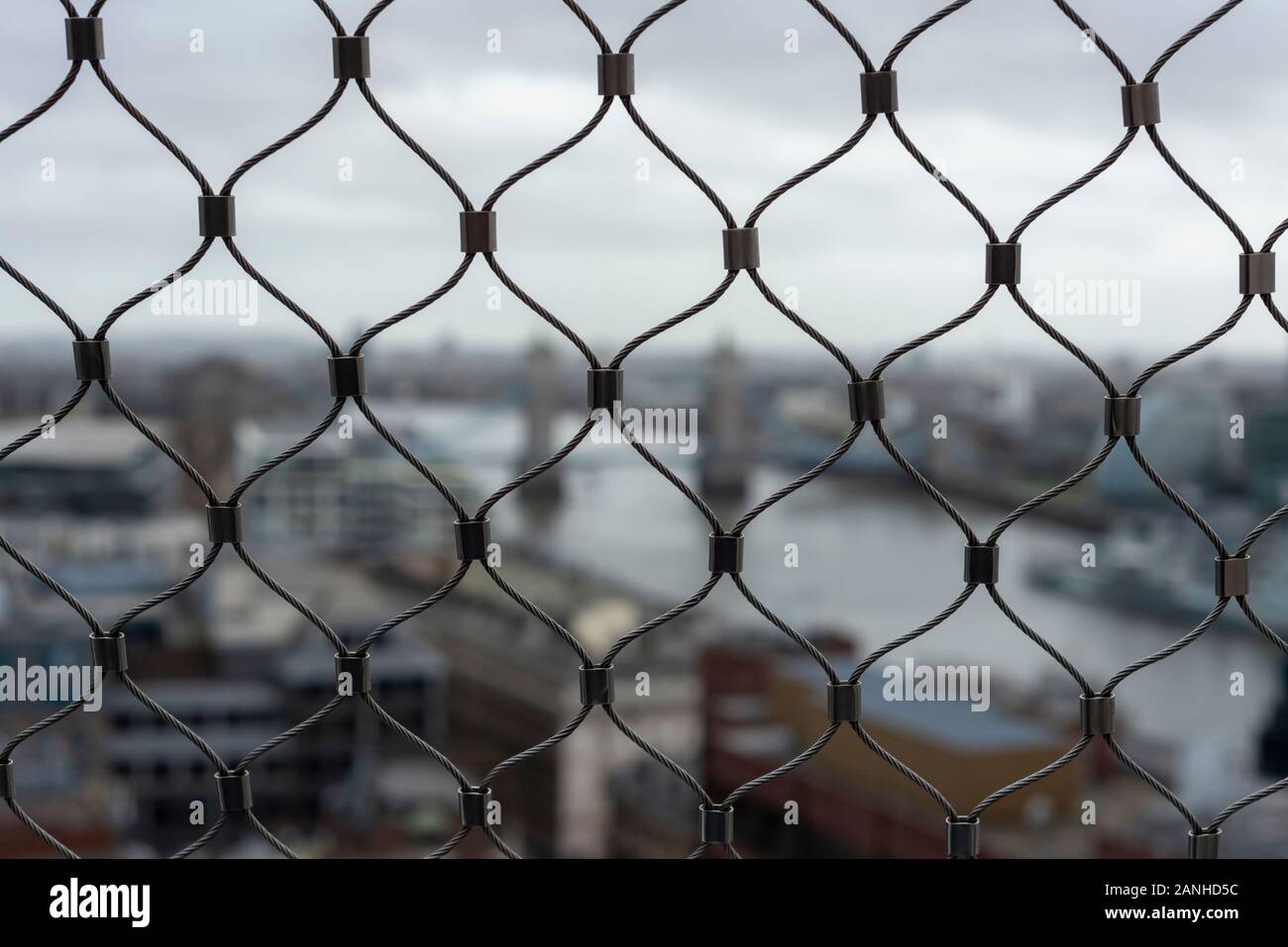 Tower Bridge London aereo 2020 come insolito sfocato vista ostruita attraverso rete di filo recinzione dalla cima del Monumento in un giorno opaco nuvoloso. Foto Stock