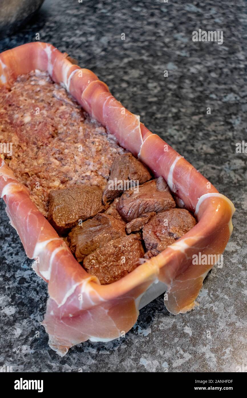 La preparazione di un gioco Terrina di carne - terrina rivestita con pancetta e riempita con carne macinata e pezzi di carne Foto Stock