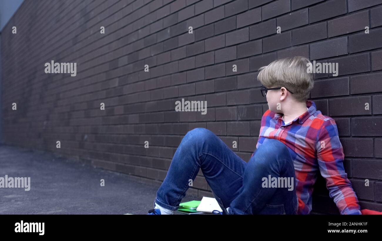 Abusato ragazzo seduto inerme vicino a parete, premuto vittima di bullismo intimidazione Foto Stock