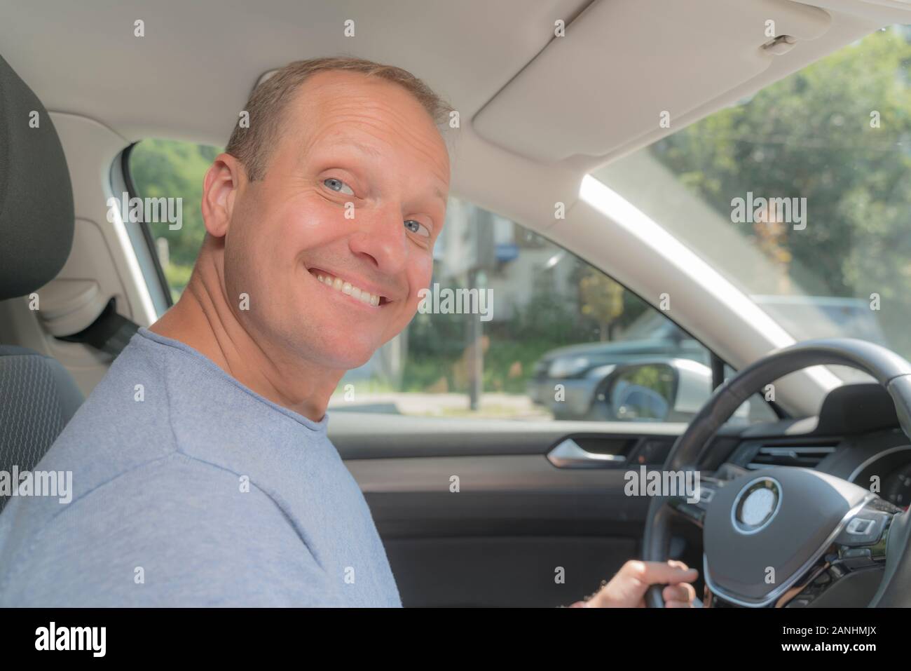 Ritratto di felice proprietario di nuova automobile, guardando la fotocamera. Bionda uomo prese una polizza di assicurazione per la sua nuova vettura, provano gioia e sorridente. Colore soffice Foto Stock