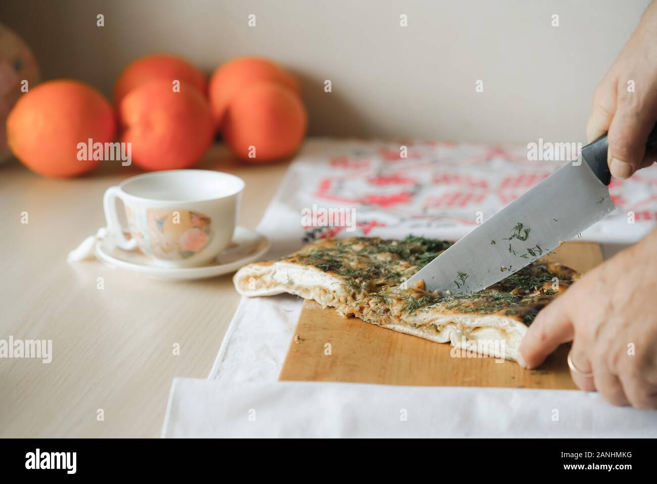 L'uomo affettare una torta di verdure con coltello da cucina sul tagliere. Sullo sfondo sono orranges e tazza da tè. In casa del cibo vegetariano concetto. Foto Stock