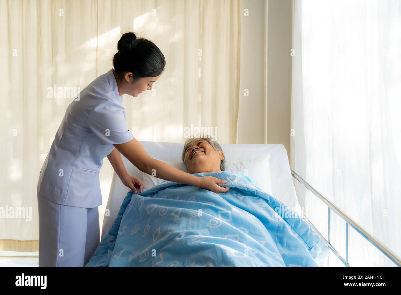 Donna anziana a letto e coperchio infermiere coperta per lei. Il vecchio donna asiatica e bella asiatica infermiera donna in camera da letto il concetto di servizio negli anziani care center Foto Stock