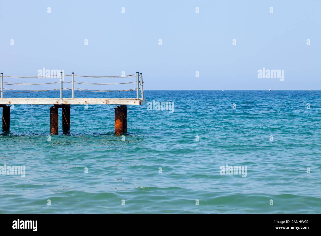 Frammento di un molo vecchio contro lo sfondo del mare blu e il cielo senza nuvole. Il romanticismo di vagabondaggi lontani. Foto Stock