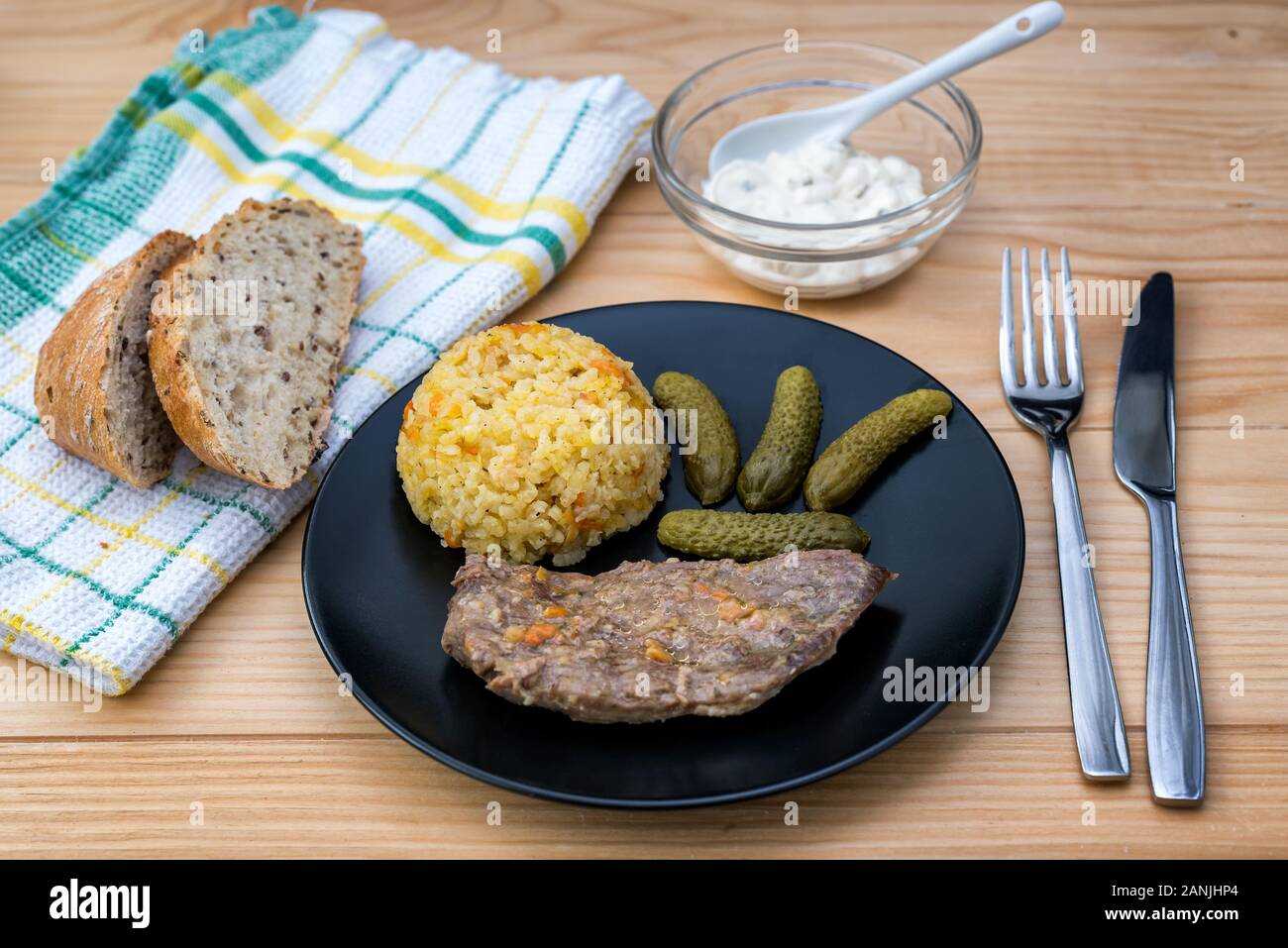 Preparate la bistecca di manzo con riso risotto, sottaceti e salsa su piastra nera sul tavolo di legno sfondo Foto Stock