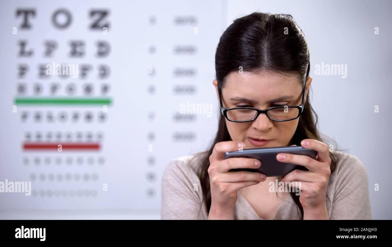 Signora gamer in occhiali la riproduzione sullo smartphone, il rischio di perdere di vista, tossicodipendenza Foto Stock