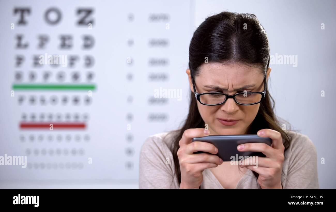 Addicted donna in occhiali la riproduzione di video gioco sullo smartphone, visione problema Foto Stock