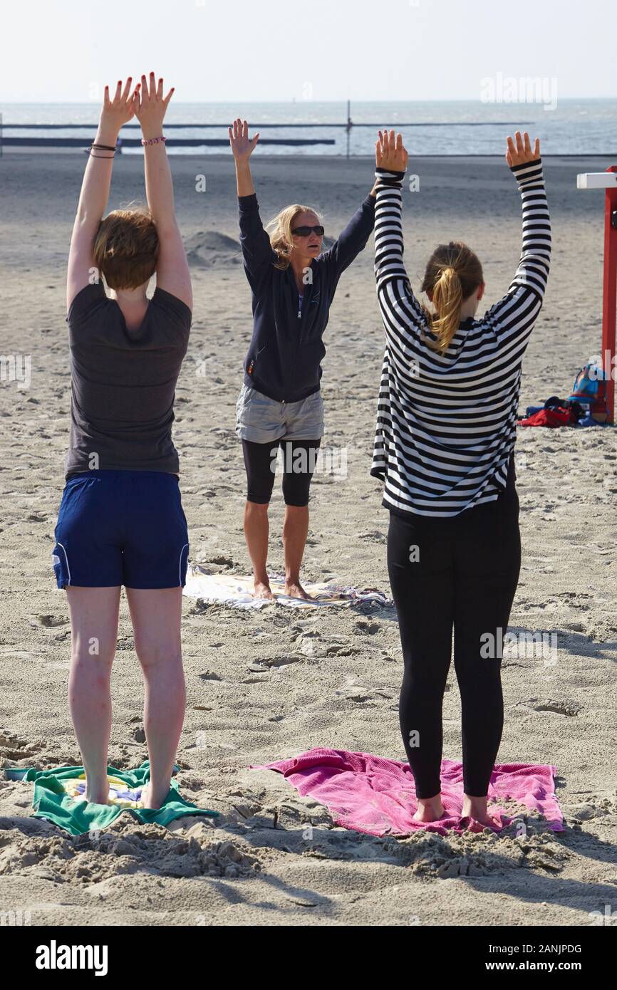 Praticante di yoga femminile che offre una lezione di yoga a un piccolo gruppo di donne sulla spiaggia meridionale dell'isola di Borkum Foto Stock