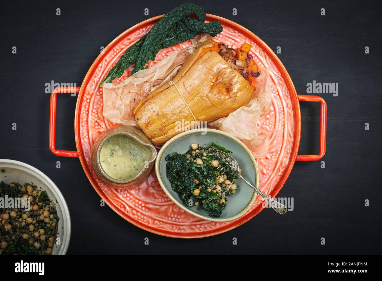 Zucca di Butternut ripiena arrosto con insalata di cavolo e ceci. Sano cibo vegano servito su un vassoio arancione con sfondo nero. Vista dall'alto / piatto Foto Stock