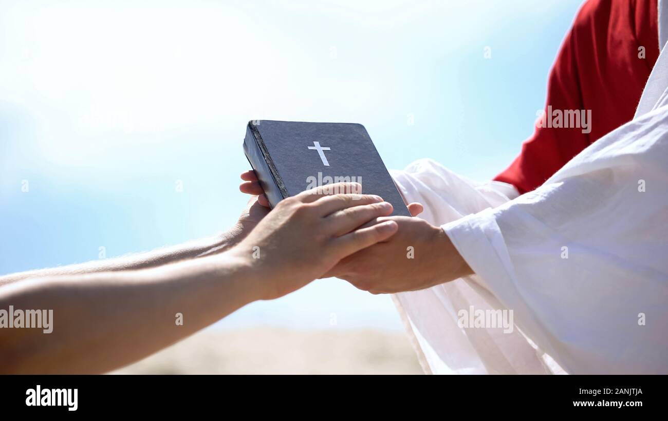 Predicatore in accappatoio passando la bibbia a mani maschili, diffondere gli insegnamenti religiosi Foto Stock