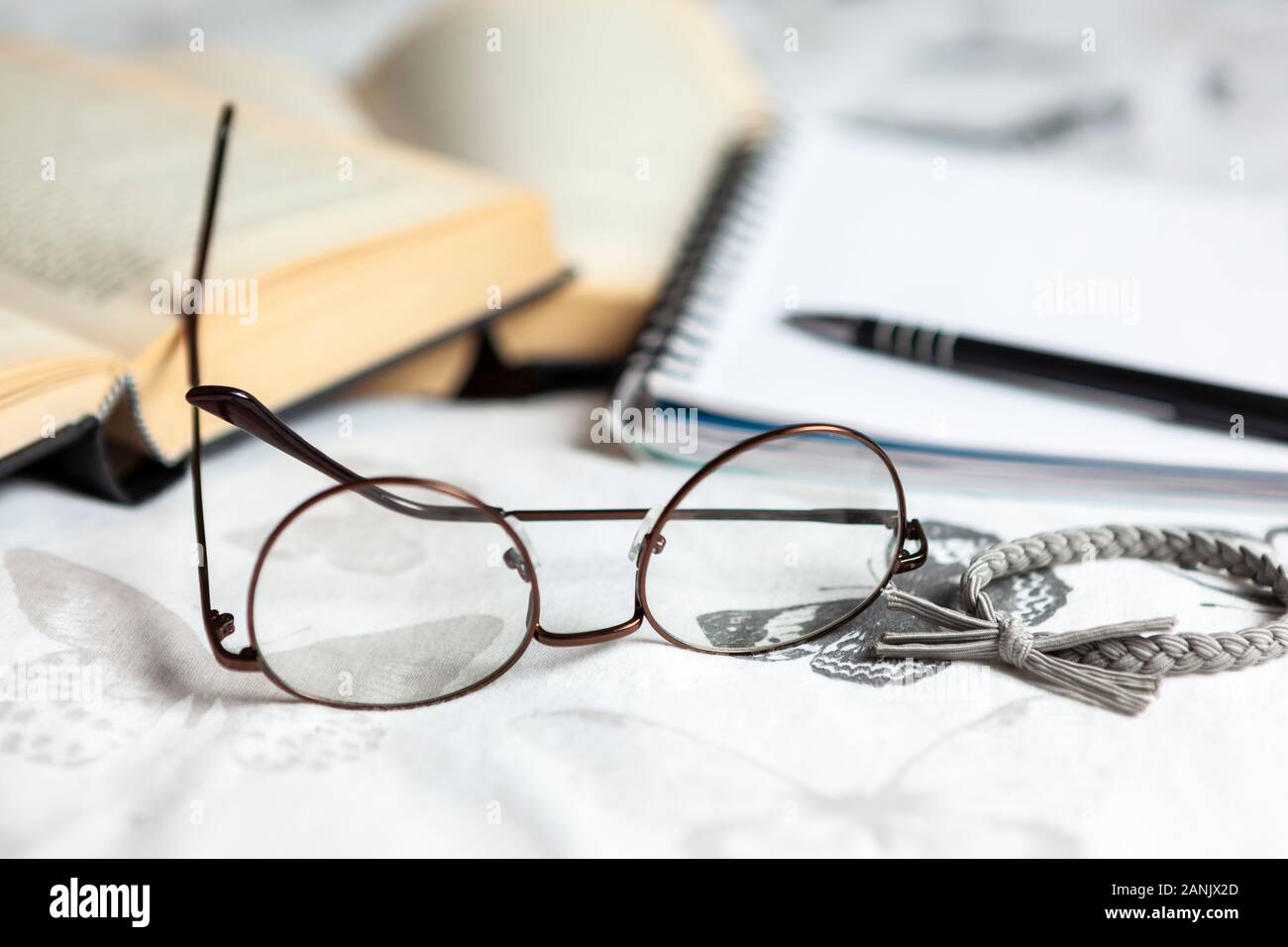 Coppia di occhiali da lettura e una fascia per capelli su un letto con alcuni libri e un blocco note Foto Stock