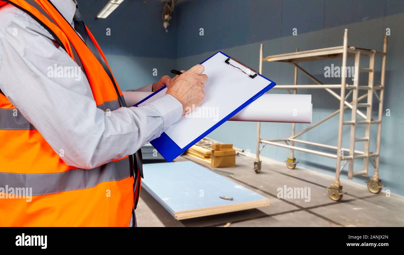 La salute e la sicurezza ufficiale in orange alta visibilità gilet di ispezione di un sito di costruzione amd scrivendo sulla sua negli appunti Foto Stock