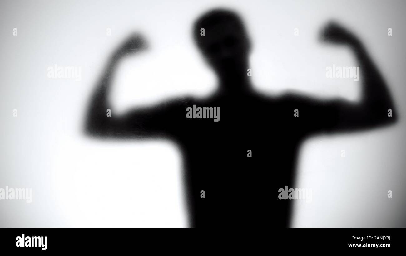 Silhouette di uomo forte che mostra bicipite dietro la parete di vetro, bodybuilding concept Foto Stock