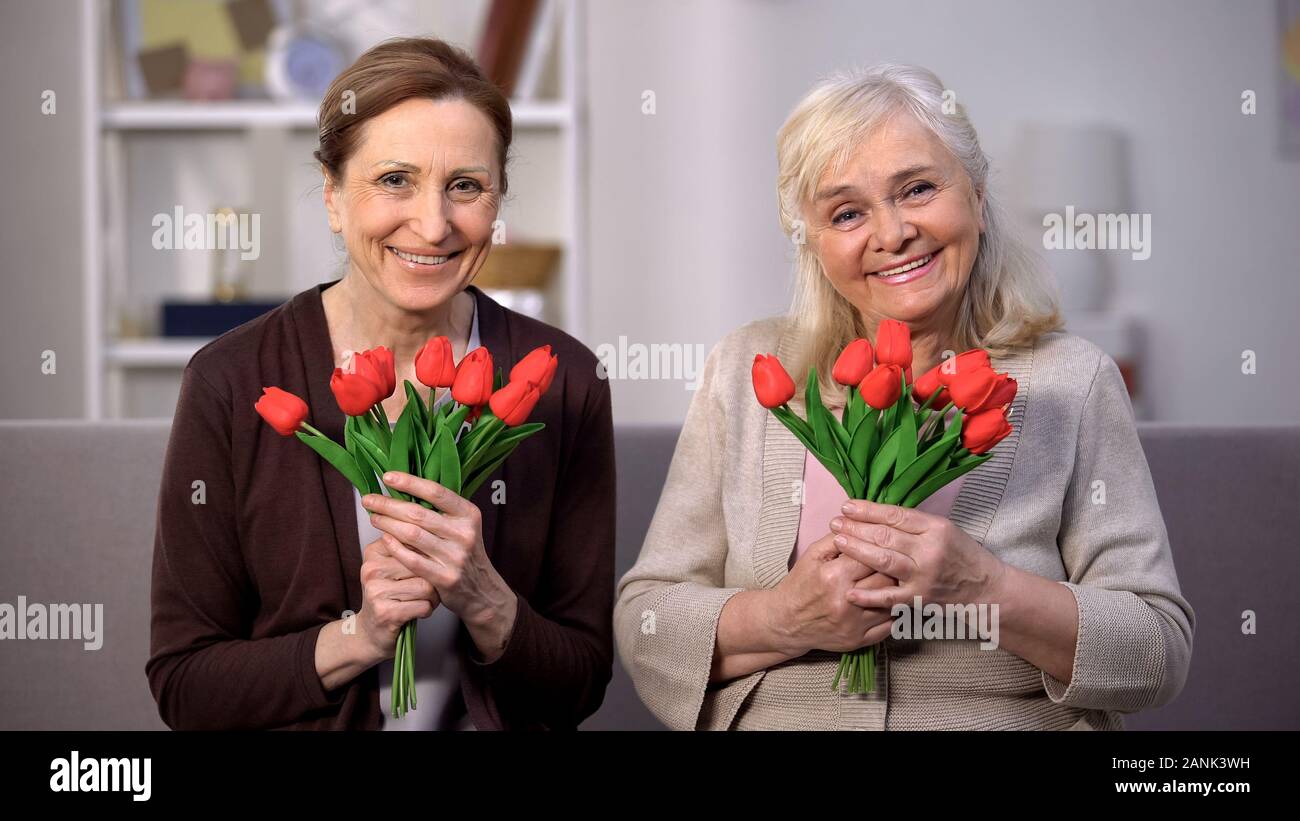 Allegro senior femmine guardando la telecamera tenendo tulipani rossi madre day celebrazione Foto Stock