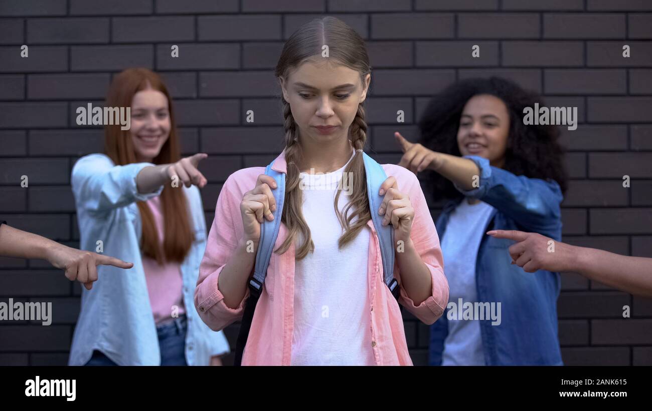 Ridere i compagni di scuola rivolta dita alla pupilla femmina con la scuola borsa, il bullismo Foto Stock