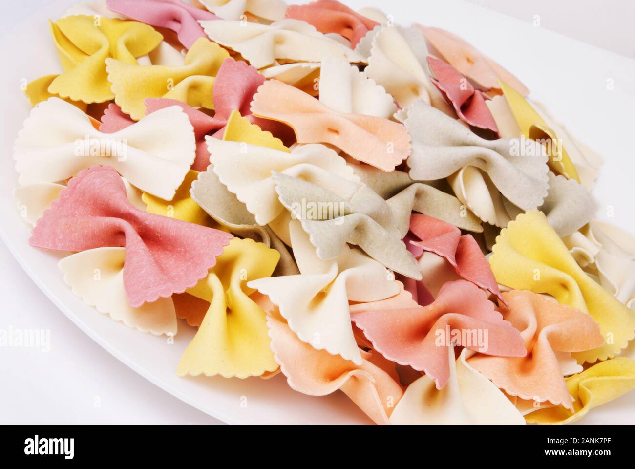 Colorati a secco il filtro bow tie italiano la pasta di semola di grano duro in una ciotola bianco. Multi colorata in giallo, rosso, bianco, arancio e grigio. Foto Stock