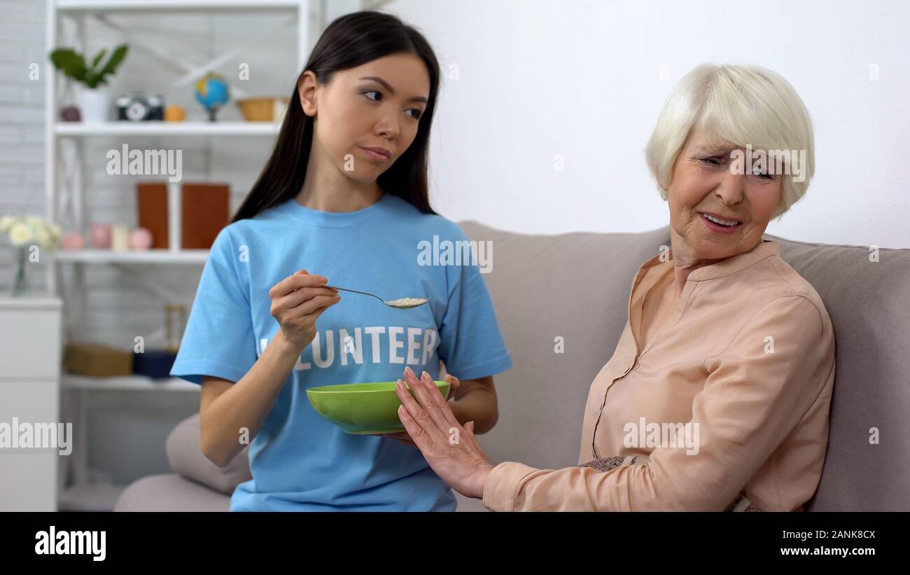 Sconvolto donna anziana che rifiuta di mangiare i fiocchi d'avena offerti da volontario, casa di cura Foto Stock