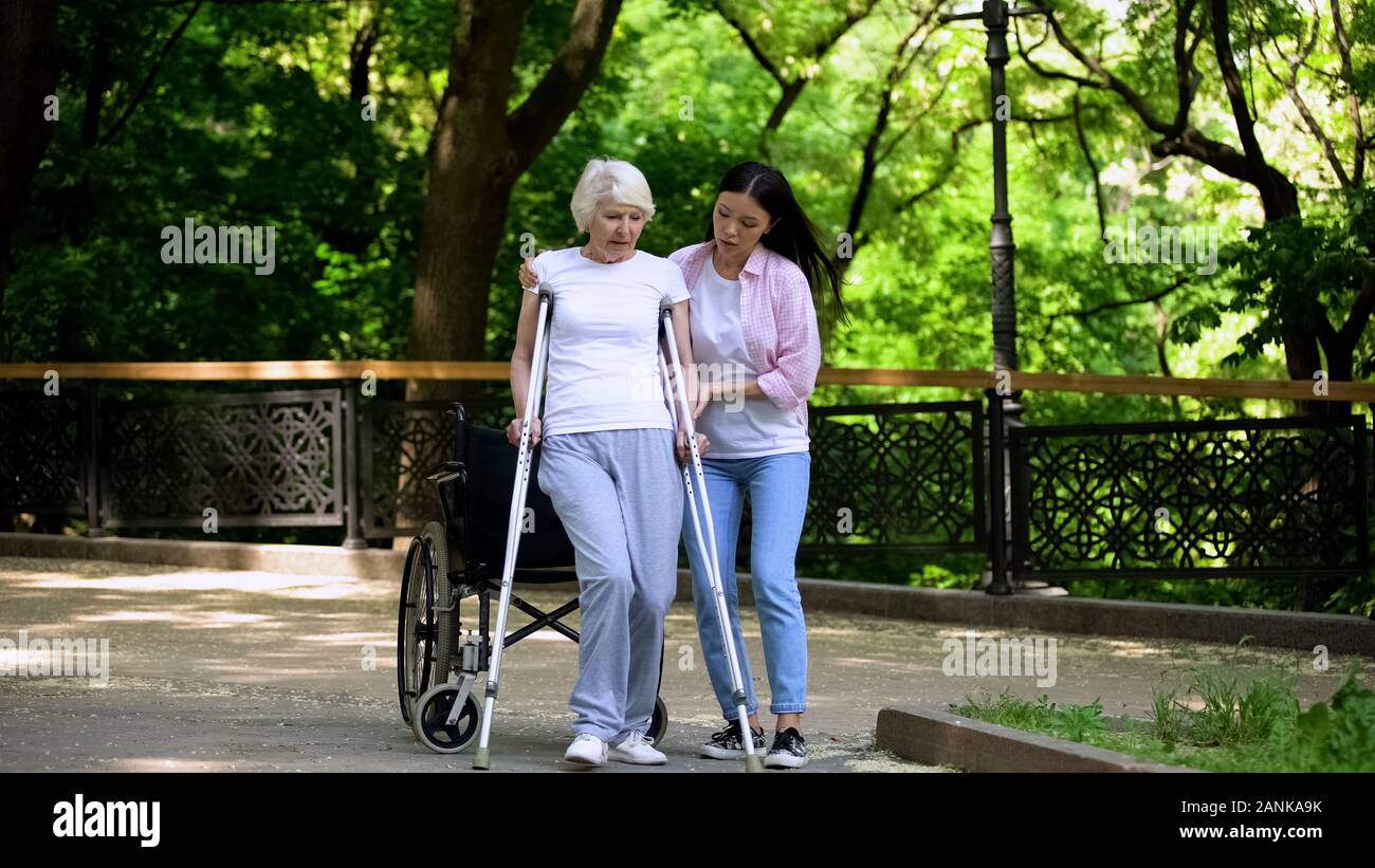 Giovane donna aiutando old Lady camminando sulle stampelle, frattura dell'anca riabilitazione Foto Stock