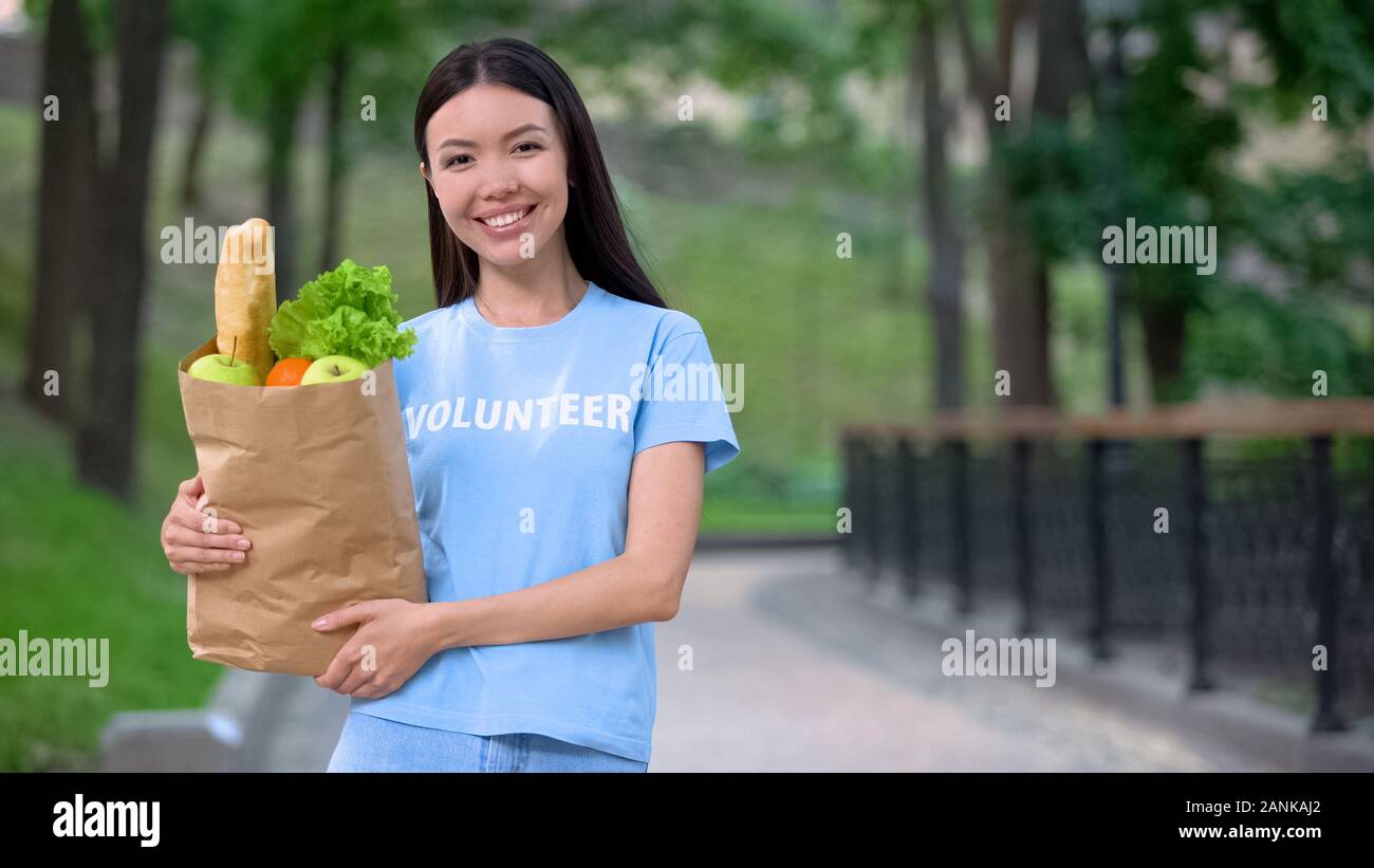 Allegro volontari femmina holding sacchetto shopper all'aperto fotocamera sorridente, donazione Foto Stock