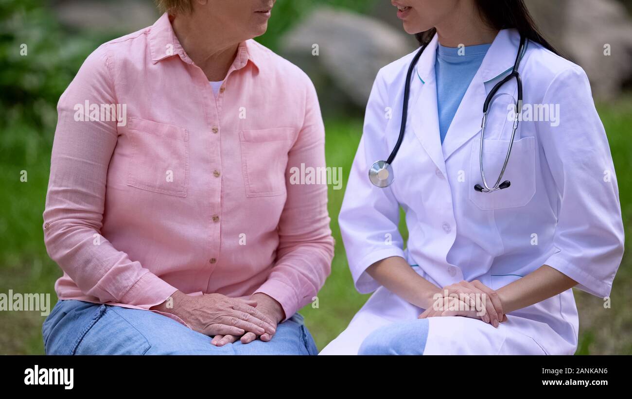 Donna anziana e medico donna parlare seduto giardino dell'ospedale, la consultazione Foto Stock