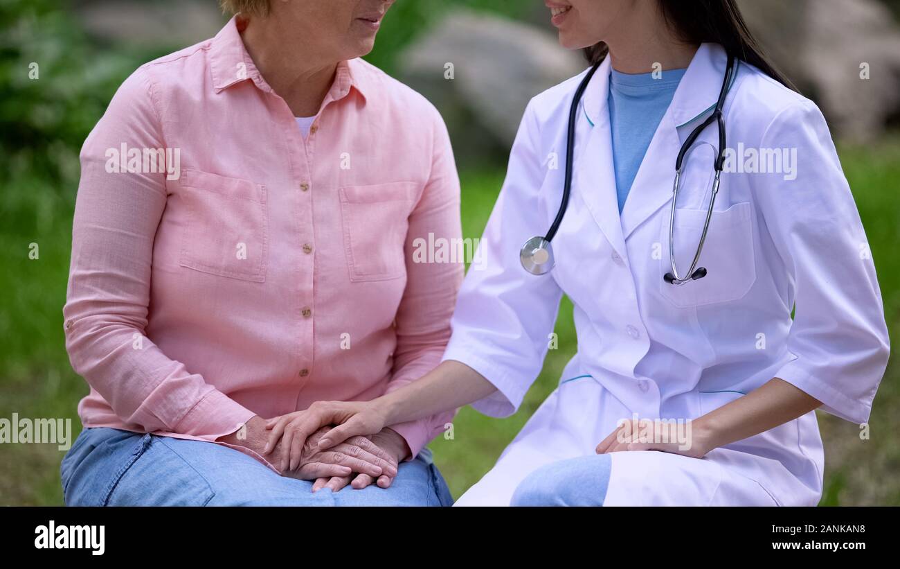 Medico donna consolante di età paziente seduto giardino dell'ospedale, clinica service Foto Stock