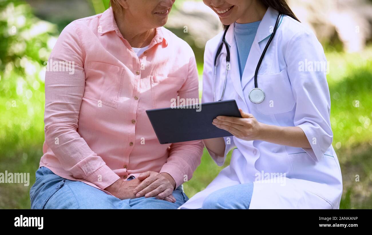 Felice medico di sesso femminile di età compresa tra paziente cercando tablet seduti all'aperto, tecnologia Foto Stock