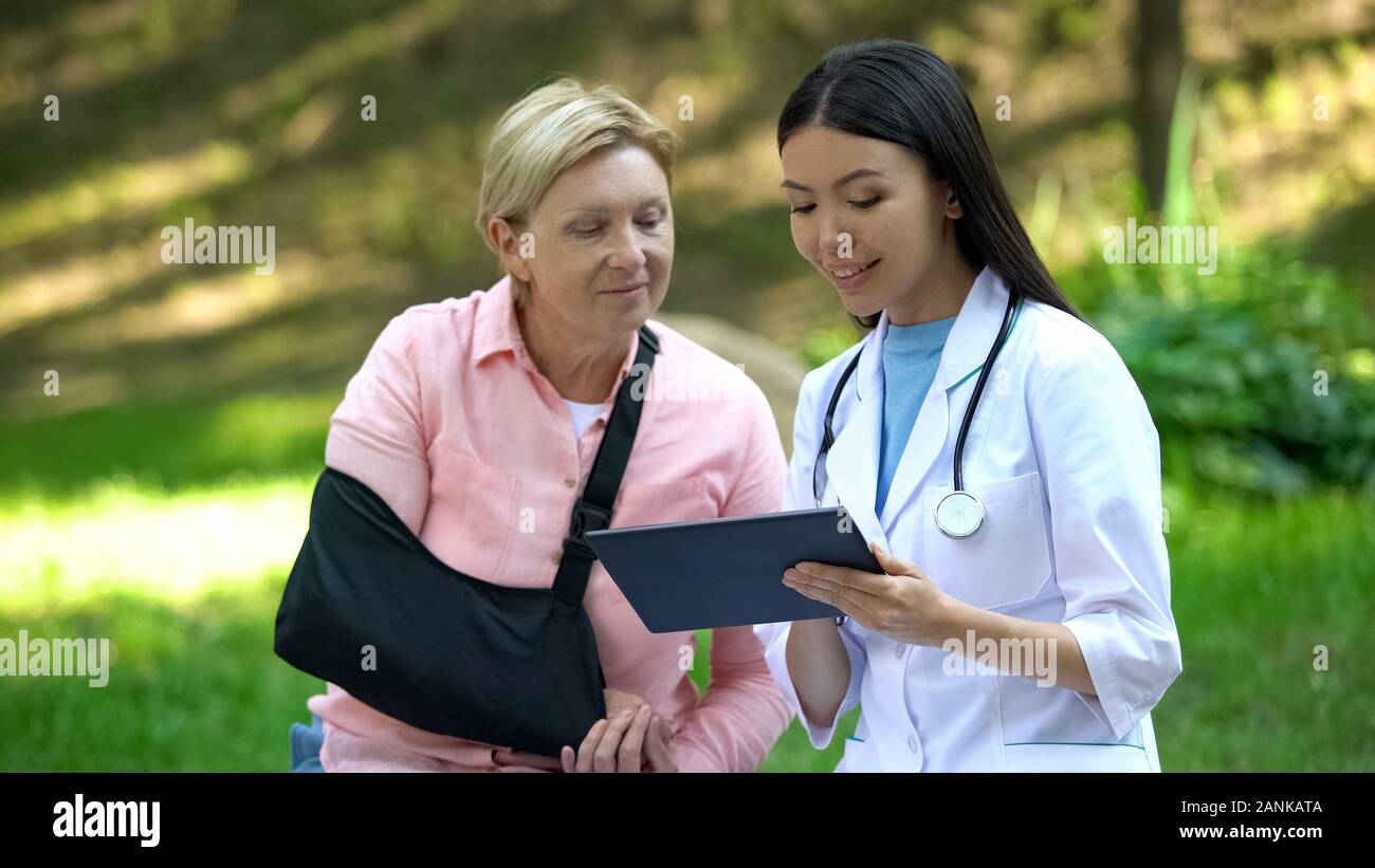 Medico Ospedaliero che mostra farmacia tablet app per senior paziente con imbracatura del braccio Foto Stock