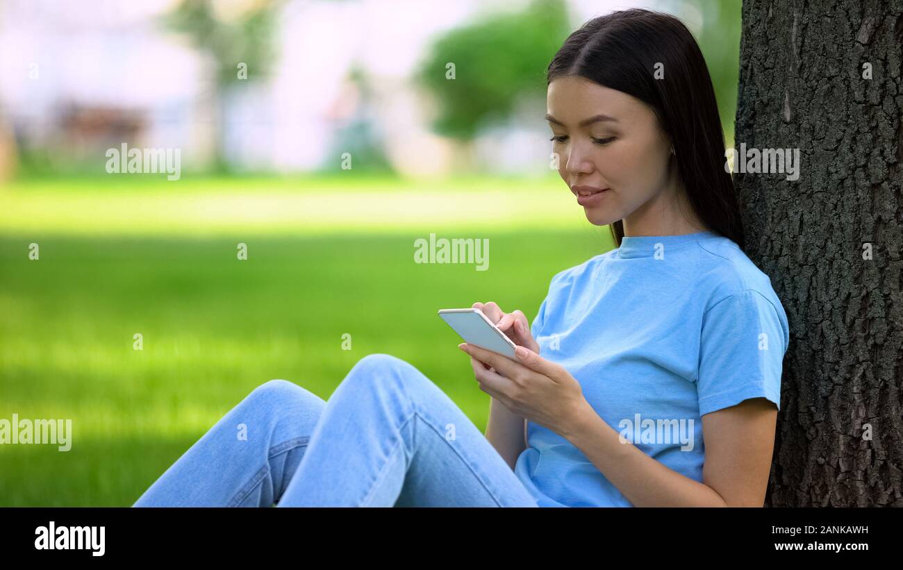Attraente giovane donna texting messaggio sullo smartphone seduti all'aperto, l'applicazione Foto Stock