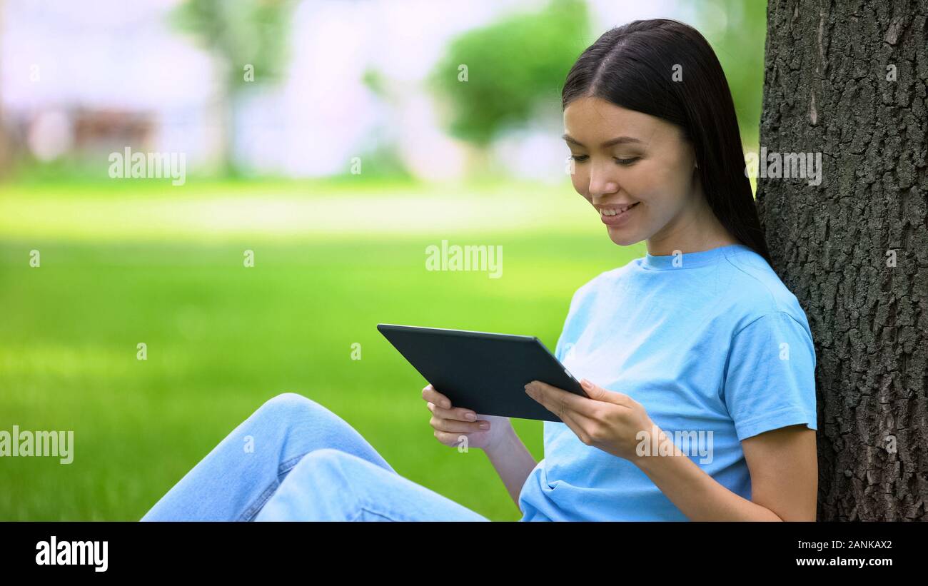 Attraente giovane donna guardando video tablet seduta park, l'applicazione on-line Foto Stock