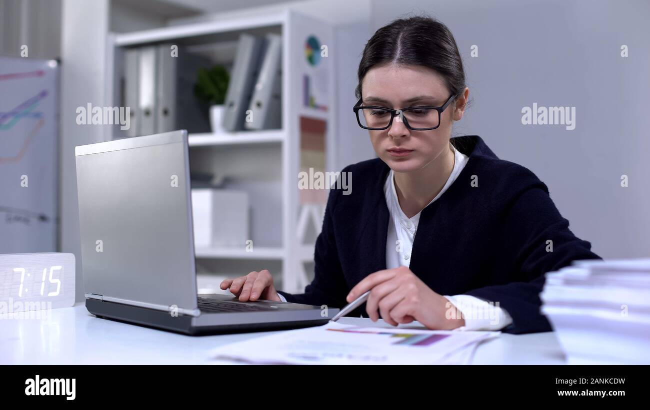 Ufficio femmina dipendente guardando attraverso le informazioni nel computer portatile e dei documenti di lavoro Foto Stock