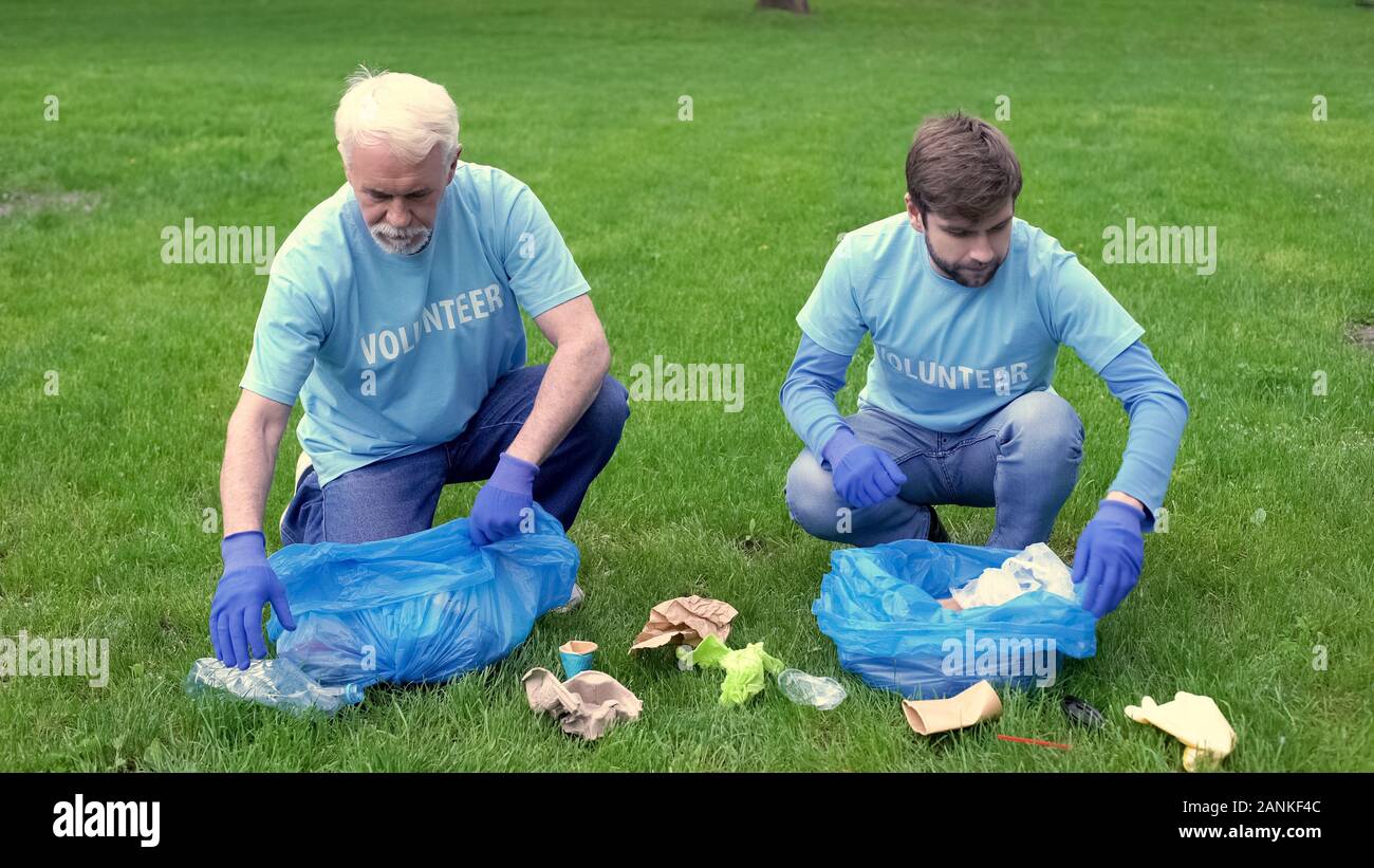 Giovani e uomini maturi nel cestino di raccolta nel sacchetto di immondizia dando alta cinque, il lavoro di squadra Foto Stock