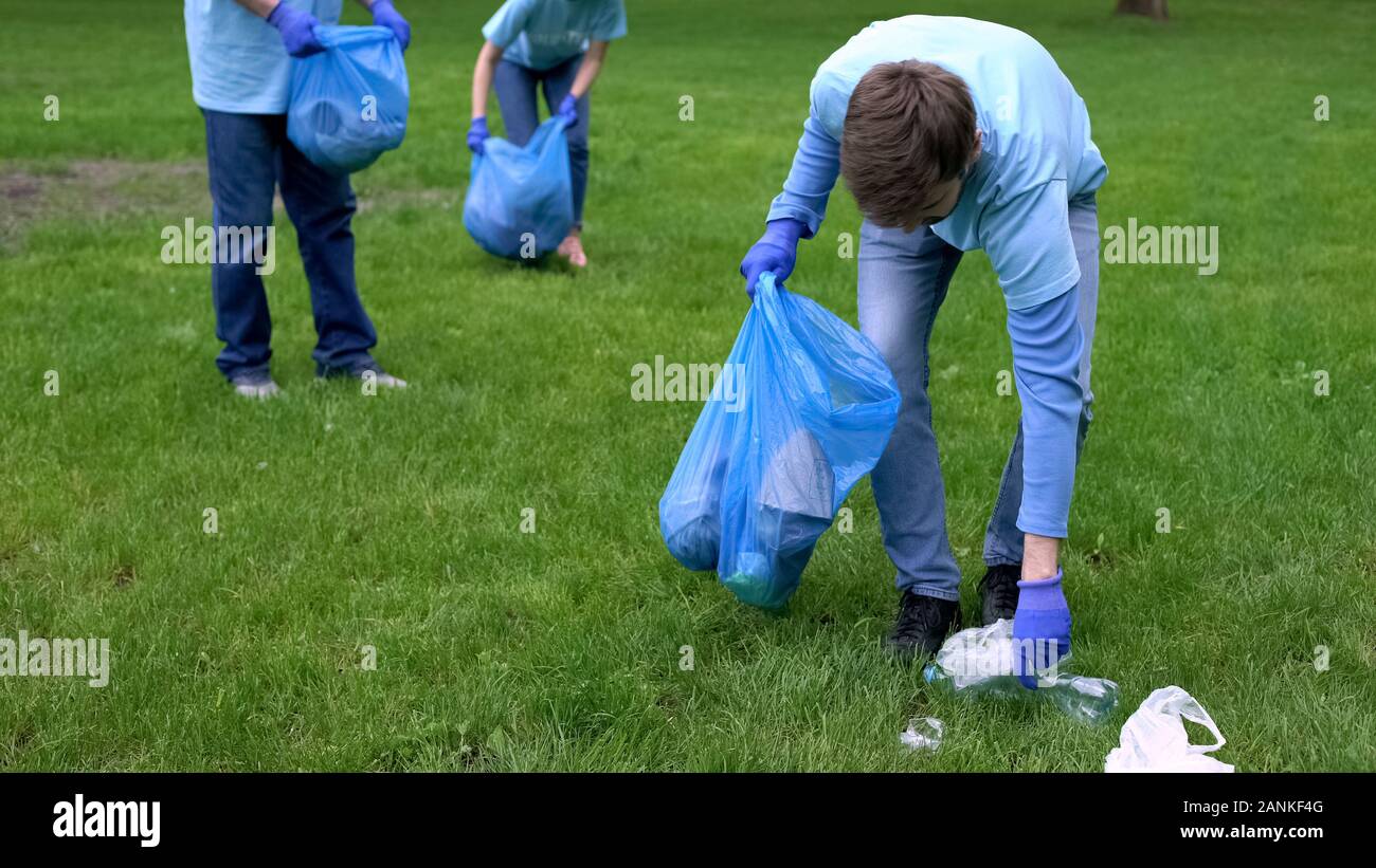 Giovani e uomini maturi nel cestino di raccolta nel sacchetto di immondizia dando alta cinque, il lavoro di squadra Foto Stock