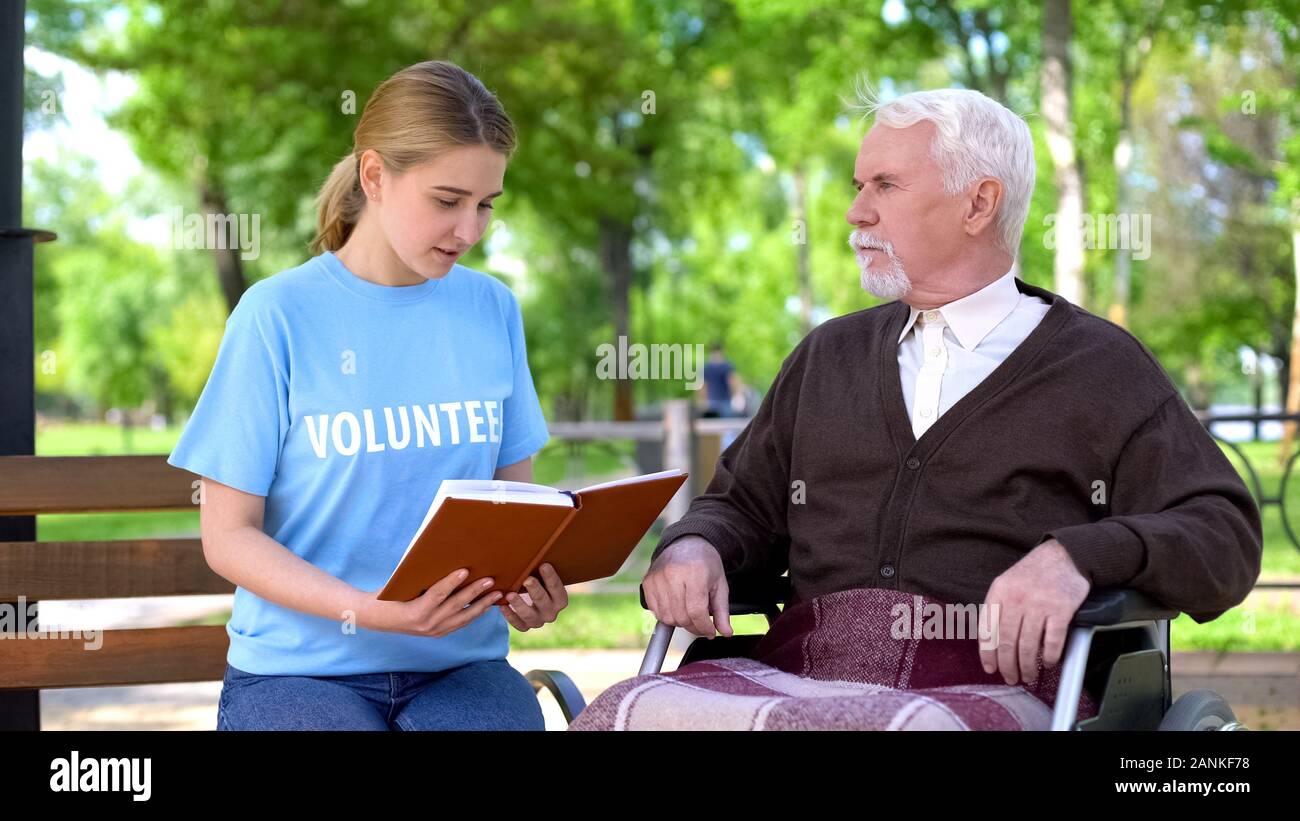 Giovani volontari femmina libro di lettura per il titolare di pensione o di rendita disabili in carrozzella, cura Foto Stock