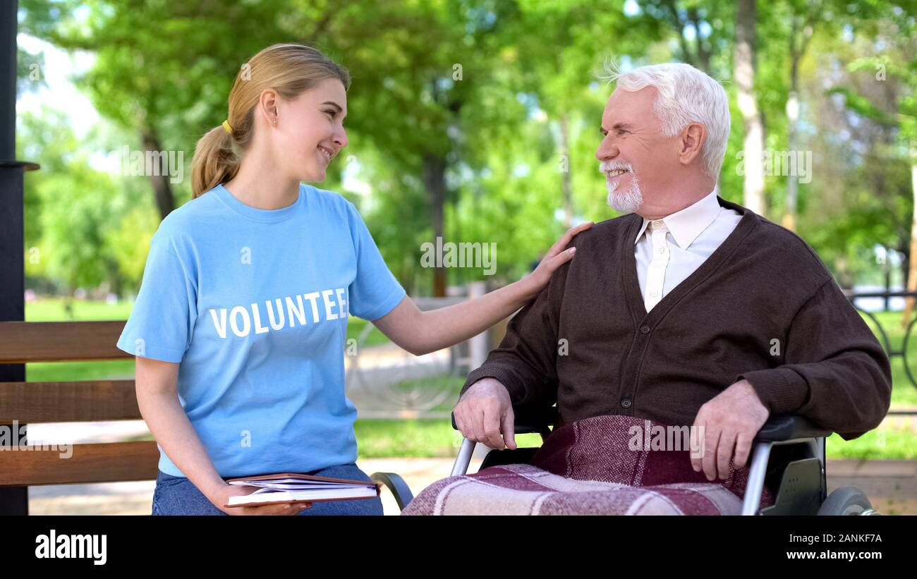 Volontari femmina azienda prenota trascorrendo del tempo con gli anziani disabili uomo in posizione di parcheggio Foto Stock