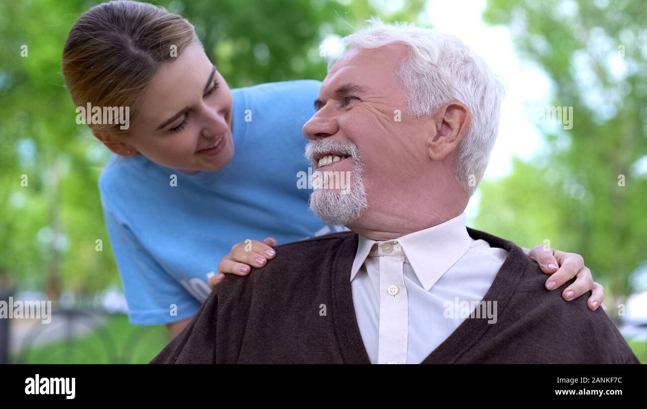 Donna sorridente volontari disabili confortante uomo anziano all'Ospedale Parco Foto Stock