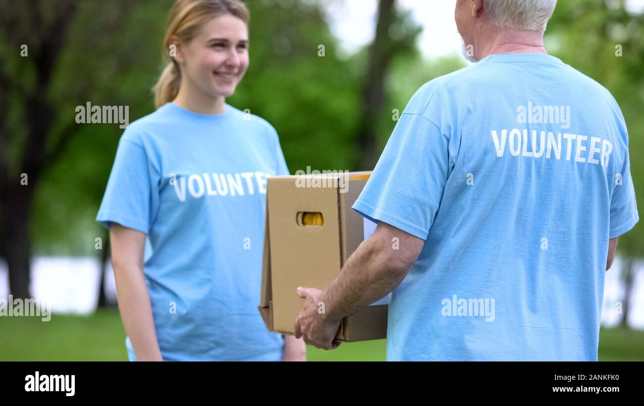 Sorridente giovane donna dando donazione casella per senior volontario, progetto di assistenza Foto Stock