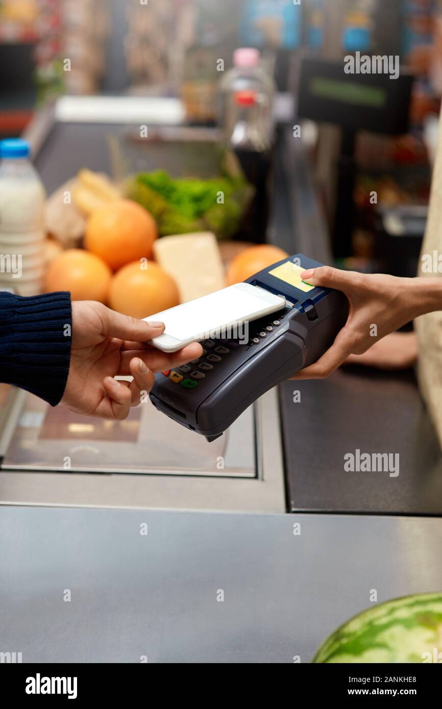 Spesa giornaliera. Uomo in piedi al supermercato contatore del cassiere di pagare per gli acquisti con lo smartphone contactless close-up Foto Stock