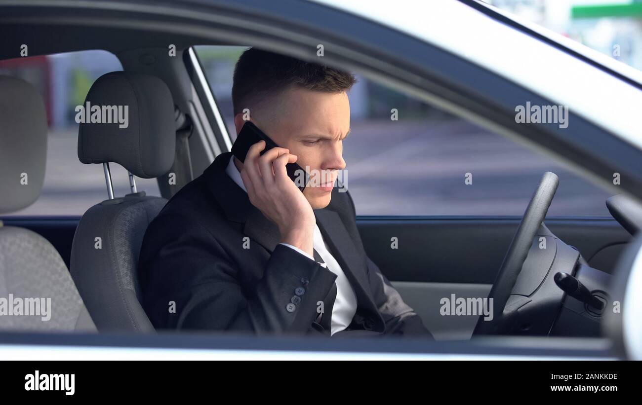 Maschio nervoso in tuta seduti sul sedile di guida e la chiamata sul telefono, in ritardo per il lavoro Foto Stock