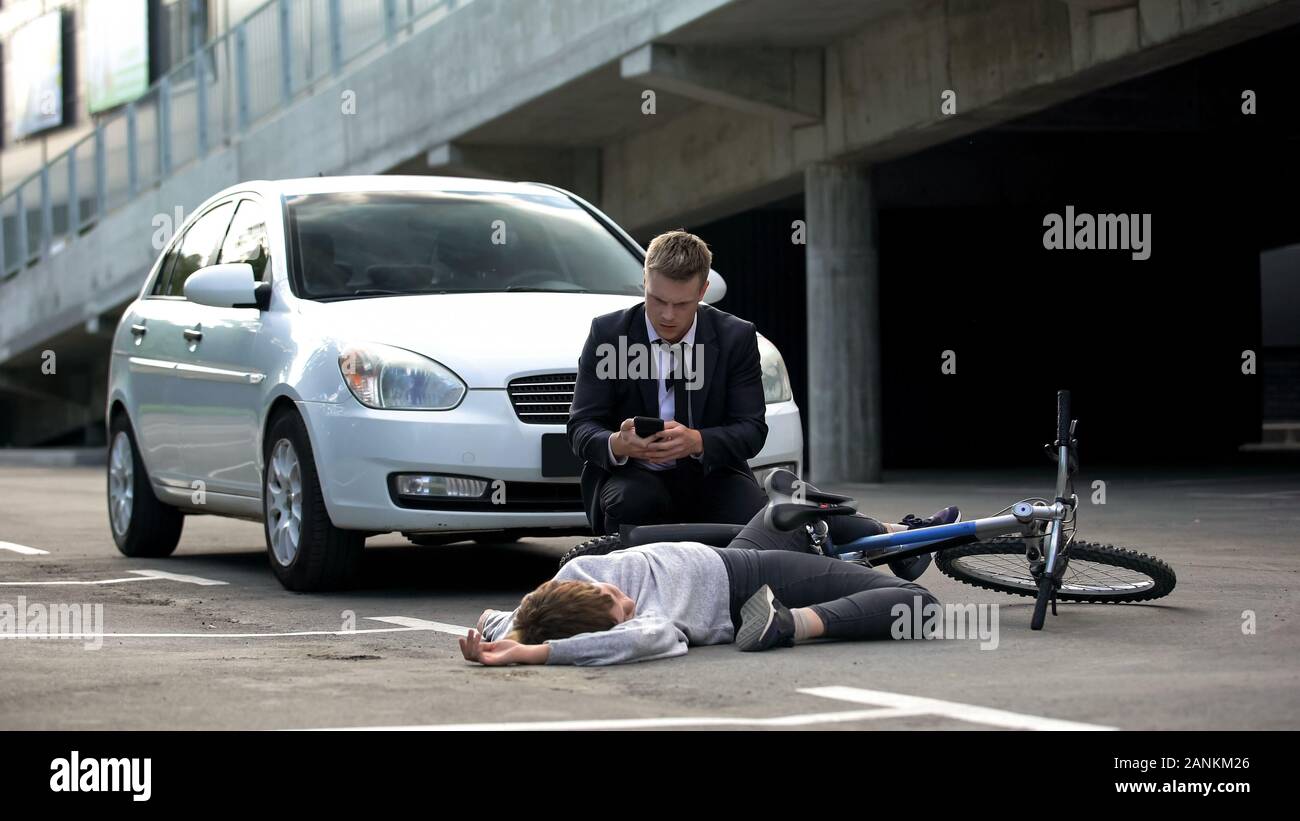 Driver maschio chiamando emergenza dopo incidente di auto, inconscio ciclista su strada Foto Stock