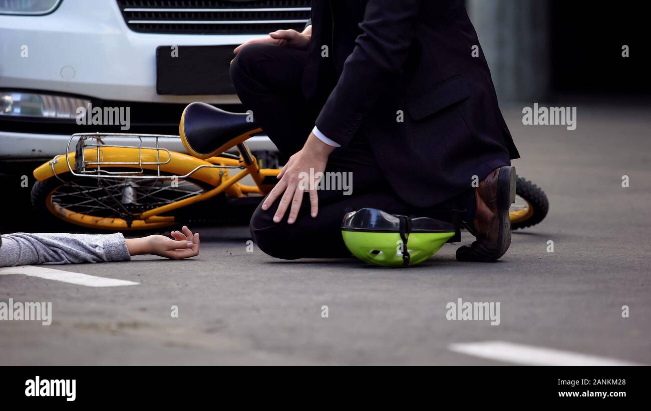Uomo in tuta vicino al ferito vittima di incidente giacente su strada, traffico di pericolo di collisione Foto Stock