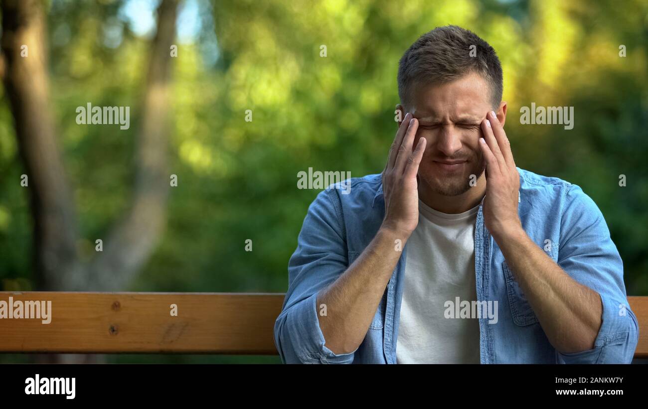 Uomo tempio massaggiante sulla panchina nel parco affetti da emicrania dolore, salute Foto Stock