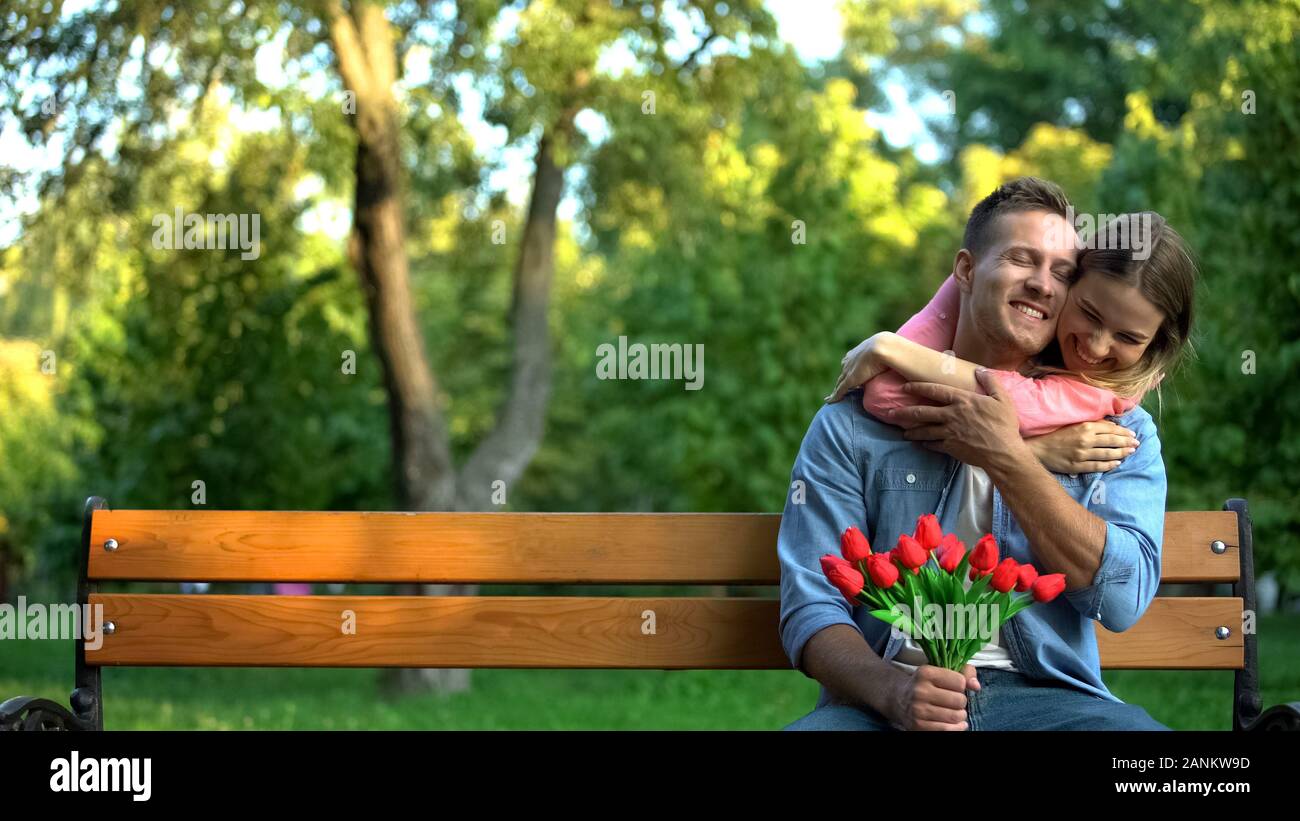 Felice giovane donna abbracciando il fidanzato holding tulipani rossi nelle mani, data all'aperto Foto Stock