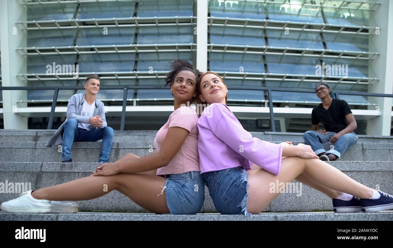 Moda teen femmine seduti a stadium, maschio amici sullo sfondo Foto Stock