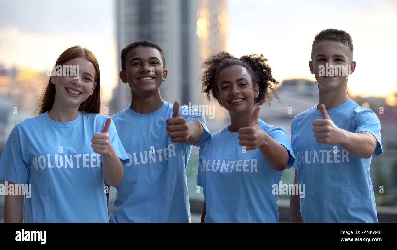 Allegro volontari che mostra Thumbs up telecamera sorridente, supporto internazionale Foto Stock