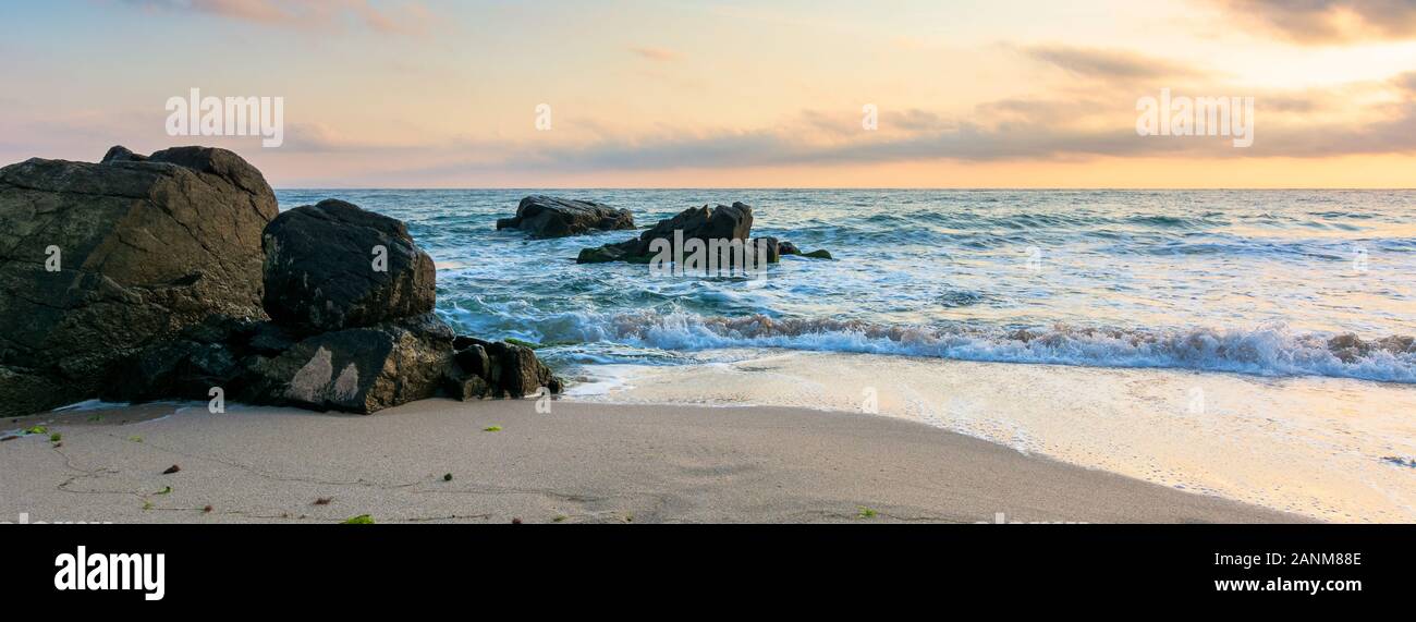 Mare spiaggia a sunrise. onde calme lavare le rocce enormi. golden nuvole sul cielo. incredibile paesaggio marino nella luce del mattino. Foto Stock