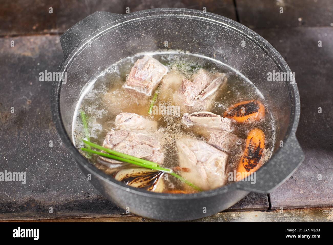 chef cuoco aggiunge gli ingredienti. brodo di manzo tradizionale con verdure, ossa e ingredienti in pentola, ricetta di cottura. Zuppa in una pentola di cottura con mestolo Foto Stock