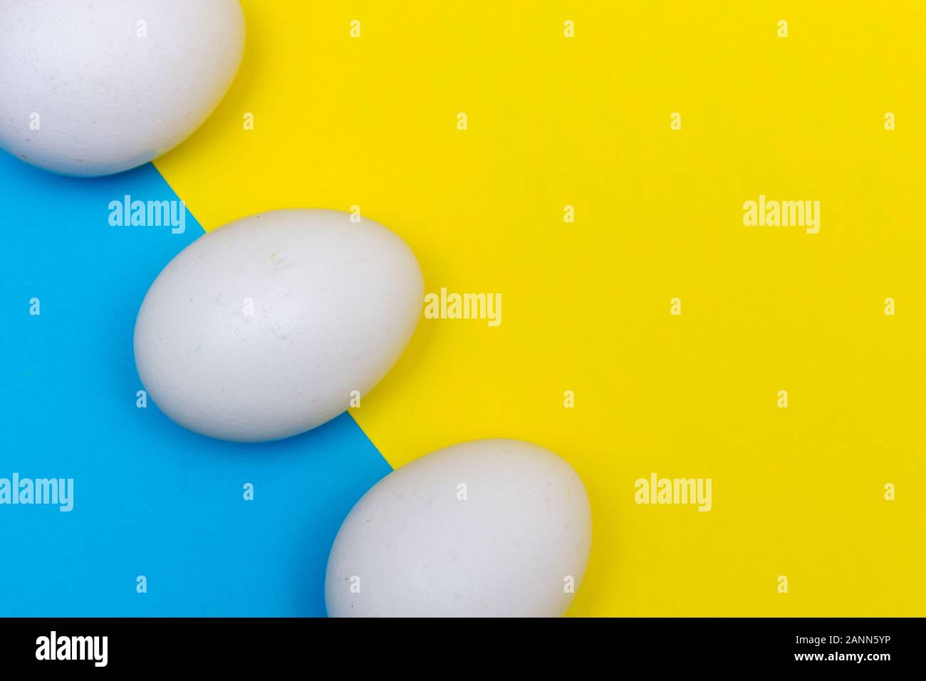 Tre vacanze di Pasqua laici piatta con uovo bianco su di un solido di colore blu chiaro e giallo vivace sfondo con copia spazio vicino. Foto Stock