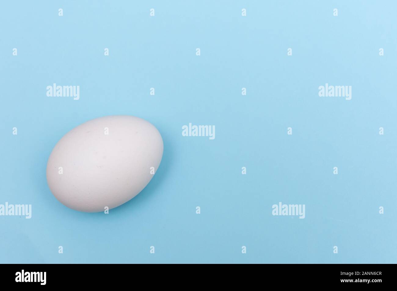 Vacanze di Pasqua laici piatta con uovo bianco su un solido azzurro pastello con sfondo spazio copia. Foto Stock
